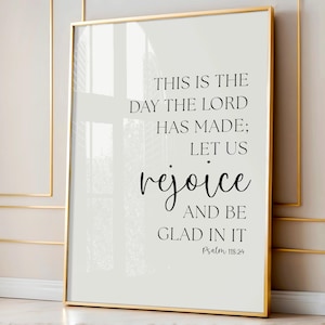 May include: A framed print with a gold border. The text reads "THIS IS THE DAY THE LORD HAS MADE; LET US rejoice AND BE GLAD IN IT" with "Psalm 118:24" at the bottom. The background is a light cream color.