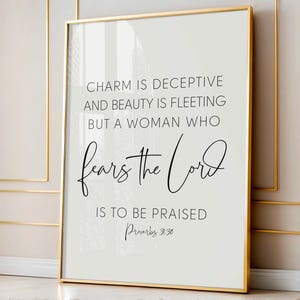 Puede incluir: Una impresión enmarcada con un borde dorado. La impresión tiene un fondo claro con texto negro que dice "CHARM IS DECEPTIVE AND BEAUTY IS FLEETING BUT A WOMAN WHO fears the Lord IS TO BE PRAISED Proverbios 31:30."
