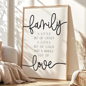 May include: A framed wall art print with the word "family" in a cursive font, followed by the phrases "A little bit of crazy, a little bit of loud, and a whole lot of love" in a black font. The frame is a light brown colour.