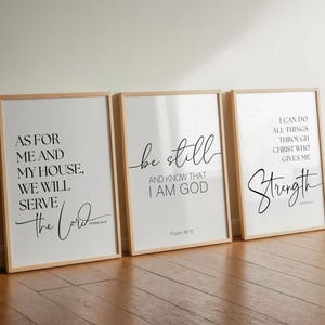 May include: Three framed art prints with inspirational quotes in black script on white backgrounds. The first reads "As for me and my house, we will serve the Lord." The second says "Be still and know that I am God." The third says "I can do all things through Christ who gives me strength."