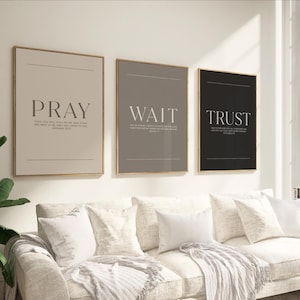 May include: Three framed wall art pieces with the words "PRAY", "WAIT", and "TRUST" in a minimalist design. The art has a neutral color palette with gold frames, suitable for home decor. The text is in a simple, elegant font.