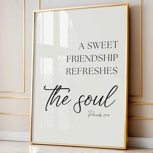 Puede incluir: Impresión enmarcada con borde dorado. La impresión presenta la cita "Una dulce amistad refresca el alma" en escritura y texto negro sobre un fondo blanco. El versículo bíblico Proverbios 27:9 está en la parte inferior.