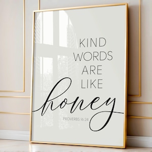 May include: A framed print with a gold border features the quote "Kind words are like honey" in black script and sans-serif fonts. The text is set against a light gray background. The Bible verse Proverbs 16:24 is below the quote.