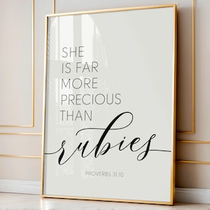 May include: A white and gray framed print with black text that reads "She is far more precious than rubies Proverbs 31:10".