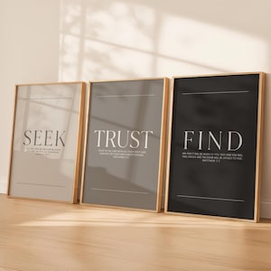 May include: Three framed art prints with gold frames. The prints feature the words "SEEK", "TRUST", and "FIND" in large white text. Each print has a different background color: beige, gray, and black. The prints also include smaller text with Bible verses.