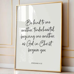 May include: A framed print with a gold border displays the text "Be kind to one another, tenderhearted, forgiving one another, as God in Christ forgave you." The text is in a handwritten style on a light grey background. The scripture reference "Ephesians 4:32" is at the bottom.