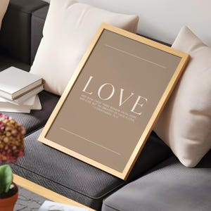 May include: A framed print with the word "LOVE" in large white letters. Below, smaller text reads "AND NOW THESE THREE REMAIN FAITH HOPE AND LOVE BUT THE GREATEST OF THESE IS LOVE 1 CORINTHIANS 13:13". The frame is gold-colored.