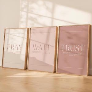 May include: Three framed prints with the words "PRAY", "WAIT", and "TRUST" in large, elegant font. The prints have a minimalist design with a neutral color palette of pink, beige, and gold. Each print includes a Bible verse.