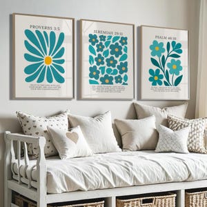 Könnte beinhalten: Drei gerahmte Kunstdrucke mit teal- und gelbblühenden floralen Designs. Jeder Druck zeigt einen anderen Bibelvers: Sprüche 3:5, Jeremia 29:11 und Psalm 46:10. Die Drucke werden über einem weißen Tagesbett mit dekorativen Kissen angezeigt.