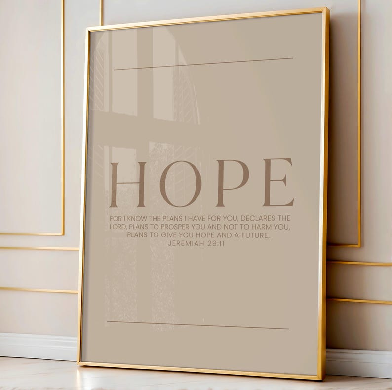 May include: A framed print with the word "HOPE" in large, brown letters. Below, a quote from Jeremiah 29:11 is printed in a smaller font. The frame is gold, and the background is a neutral beige color.