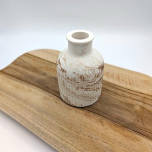 Peut inclure: Un petit vase en céramique blanche avec des marbrures brunes et un design côtelé. Le vase est posé sur une surface en bois.