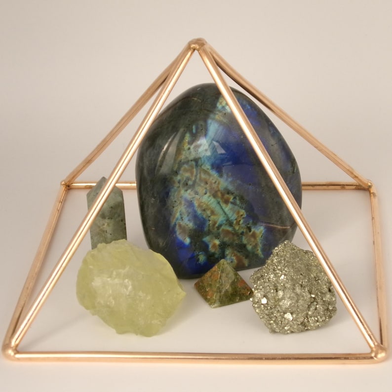 May include: A copper-colored wire pyramid frame enclosing a collection of natural stones, including a large polished dark blue labradorite, a pale yellow raw crystal, a small green pyramid, a tiny grey point, and a cluster of metallic pyrite.