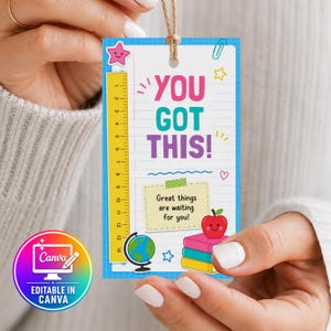 May include: A rectangular paper tag with a blue grid border featuring the text YOU GOT THIS! in pink, teal, and purple. It includes a yellow ruler marked 1 to 14 inches, a globe, a stack of books with a red apple, and a note saying Great things are waiting for you!
