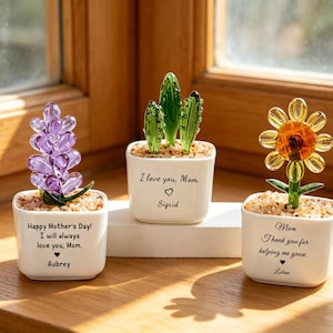 May include: Three glass flower sculptures in white square pots. A purple lavender, a green cactus, and a yellow sunflower are displayed. Each pot has a message: "Happy Mother's Day! I will always love you, Mom. Aubrey", "I love you, Mom. Sigrid", and "Mom, Thank you for helping me grow. Latter."