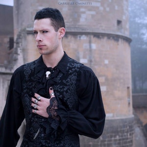 A goth male model wearing a resin raven skull necklace handmade by a skull jewelry artist. The style of the necklace is alternative gothic fashion for Halloween or a gift. The bone jewelry pendant is brown with a black beak, like a real animal skull.