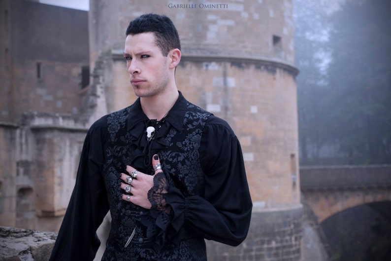 A goth male model wearing a resin raven skull necklace handmade by a skull jewelry artist. The style of the necklace is alternative gothic fashion for Halloween or a gift. The bone jewelry pendant is brown with a black beak, like a real animal skull.