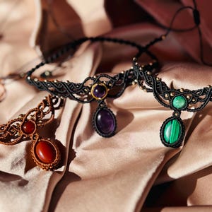 May include: Three handmade macrame necklaces with gemstone pendants. The necklaces are made with black, brown, and gold cord. The pendants are amethyst, malachite, and carnelian.