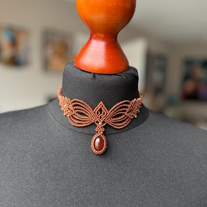 Op de afbeelding: Een bruine macramé choker ketting met een druppelvormige hanger van carneol.