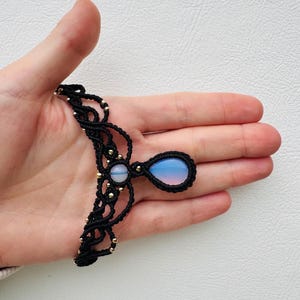 May include: A black macrame necklace with a teardrop-shaped blue and pink gemstone pendant.