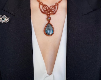Puede incluir: Un collar de macramé marrón con un colgante de piedra de labradorita en forma de lágrima. El collar presenta un diseño delicado e intrincado y está adornado con piedras preciosas más pequeñas.