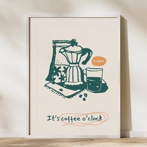Op de afbeelding: Een ingelijste kunstdruk met een groen en oranje illustratie van een koffiezetapparaat, een glas koffie en koffiebonen. De tekst "It's coffee o'clock" staat eronder. Het kunstwerk staat tegen een crèmekleurige achtergrond.