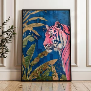 Op de afbeelding: Kunstprint in een zwarte lijst, met een roze tijger met zwarte strepen op een blauwe achtergrond. Goudblad details en groene bananenbladeren dragen bij aan het exotische thema. Een opvallend kunstwerk voor thuis.