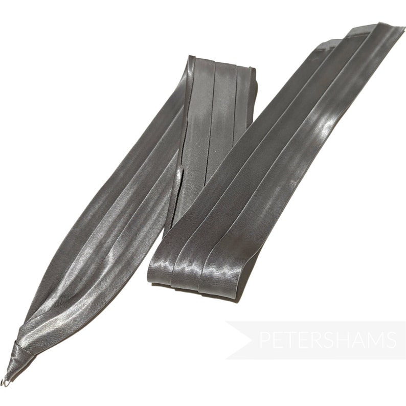 May include: A silver satin ribbon folded in a decorative way. The ribbon is about 1 inch wide and has a subtle sheen.