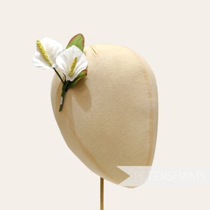 May include: A white flower hair clip with two white flowers and green leaves. The flowers have a gold center.