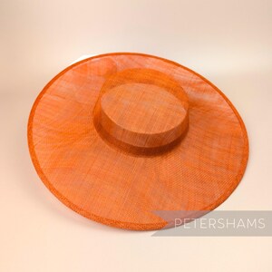 May include: A large, wide-brimmed hat made of orange straw with a smaller, round crown. The hat has a subtle texture and a slightly curved brim.