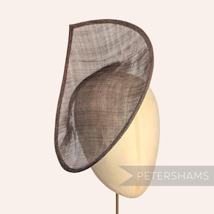 Pode incluir: Um chapéu marrom assimétrico com um design de malha, exibido em uma cabeça de manequim. O chapéu tem uma borda marrom escura e um interior marrom claro. O texto "PETERSHAMS" é visível no canto inferior direito.