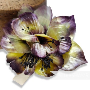 May include: A yellow and purple velvet flower with black stamens. The flower is made of fabric and has a delicate, layered design.