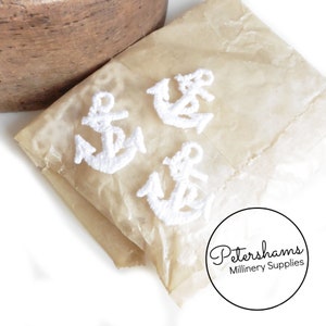 May include: Four white embroidered anchor shapes on a brown paper bag. The bag has the text "Petershams Millinery Supplies" printed on it.