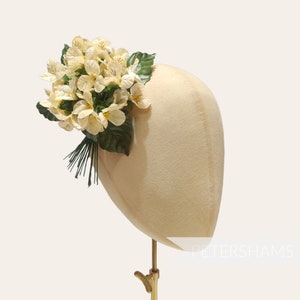 Könnte beinhalten: Ein weißer Mannequin-Kopf mit einem Blumenhaarschmuck aus weißen Blüten und grünen Blättern.