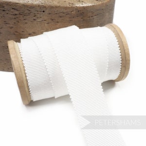 May include: White grosgrain ribbon wound around a wooden spool. This ribbon is a classic, versatile trim for sewing and crafting projects.