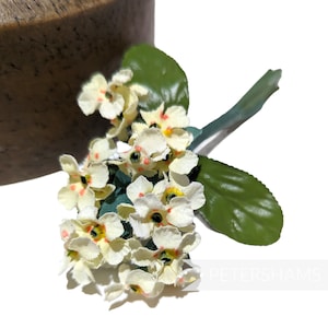 Può includere: Un gruppo di piccoli fiori di stoffa bianchi con centri arancioni. I fiori sono disposti su uno stelo verde con due foglie.