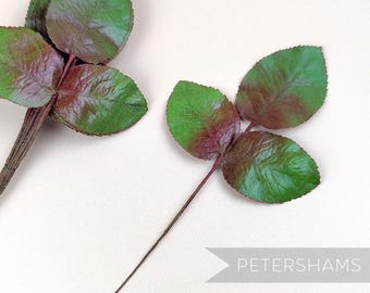 May include: Two sprigs of artificial rose leaves with a green and burgundy color. The leaves are made of fabric and have a realistic appearance.
