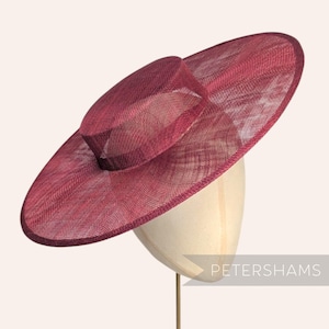 May include: A burgundy-colored hat with a wide brim and a smaller, raised crown. The hat is made of a woven material and is displayed on a mannequin head. The word "PETERSHAMS" is visible in the lower right corner.