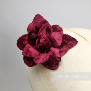May include: A large, burgundy velvet flower with a single stem and leaves. The flower is made of multiple layers of petals and has a soft, plush texture.
