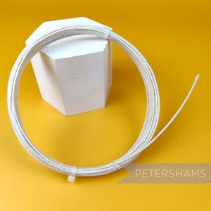 Könnte beinhalten: Eine Spule mit weißem gewachstem Leinenfaden, etwa 91 Meter lang, auf einem weißen achteckigen Sockel. Der Faden wird für Bastelarbeiten, Schmuckherstellung und andere Projekte verwendet.