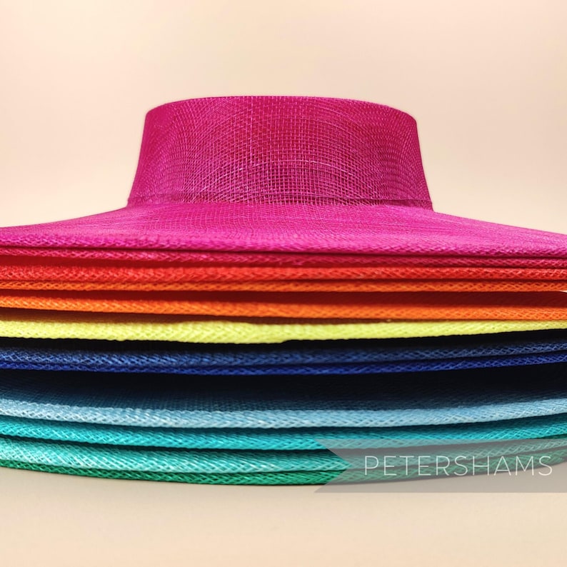 May include: A stack of colourful, wide-brimmed hats made of woven straw. The hats are arranged in a rainbow pattern, starting with a bright pink hat at the top and ending with a green hat at the bottom.