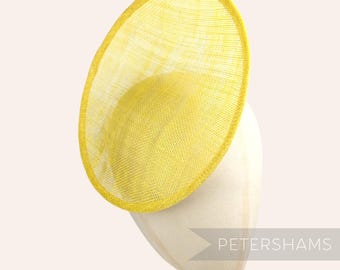 May include: A bright yellow, round, wide-brimmed hat made of woven straw. The hat is sitting on a white hat stand.