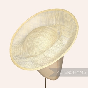 May include: A cream-colored, wide-brimmed hat with a rounded crown and a slightly angled brim. The hat is made of a woven material, and the brim has a delicate, airy appearance. The hat is displayed on a mannequin head.