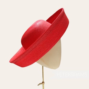 May include: A vibrant red sun hat with a wide brim and a structured crown. The hat is displayed on a mannequin head, showcasing its shape and design. The hat's texture appears woven, suggesting a lightweight material.