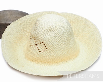 May include: A cream-colored straw hat with a wide brim and a heart-shaped design on the crown. The hat is made of woven straw and has a slightly textured surface.