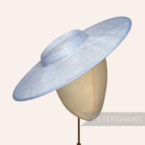 Op de afbeelding: Een lichtblauwe hoed met brede rand, met een ronde kroon en een brede, cirkelvormige rand. De hoed is gemaakt van een geweven materiaal en wordt op een mannequinhoofd getoond. De kleur van de hoed is een zacht, pastelblauw.