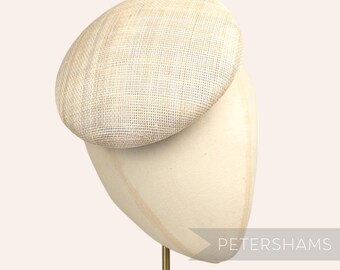May include: A small, round, off-white hat made of woven straw. The hat is sitting on a white hat stand. The hat stand has a gold metal rod.