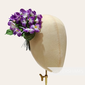 Könnte beinhalten: Ein Haarschmuck mit lila und weißen Blüten und grünen Blättern, auf einem beigefarbenen Mannequin-Kopf ausgestellt.