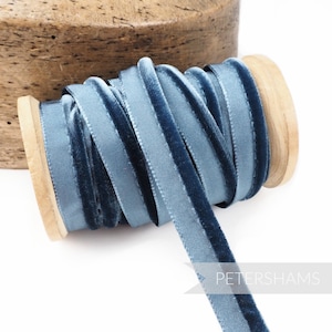 Könnte beinhalten: Eine Spule mit blauem Samtband mit Satinrand. Das Band ist um eine Holzspule gewickelt.