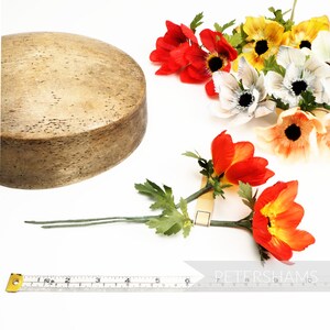 May include: A wooden round base with a light brown finish and a set of artificial flowers with red, orange, white, and yellow petals. The flowers are arranged in a bouquet with green leaves.