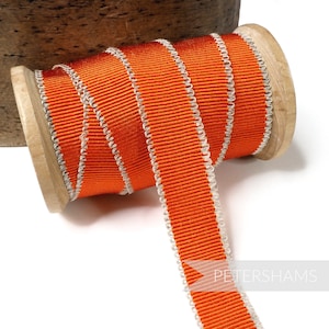 Könnte beinhalten: Eine Spule mit orangefarbenem Grosgrainband mit weißem Paspel. Das Band ist um eine Holzspule gewickelt.